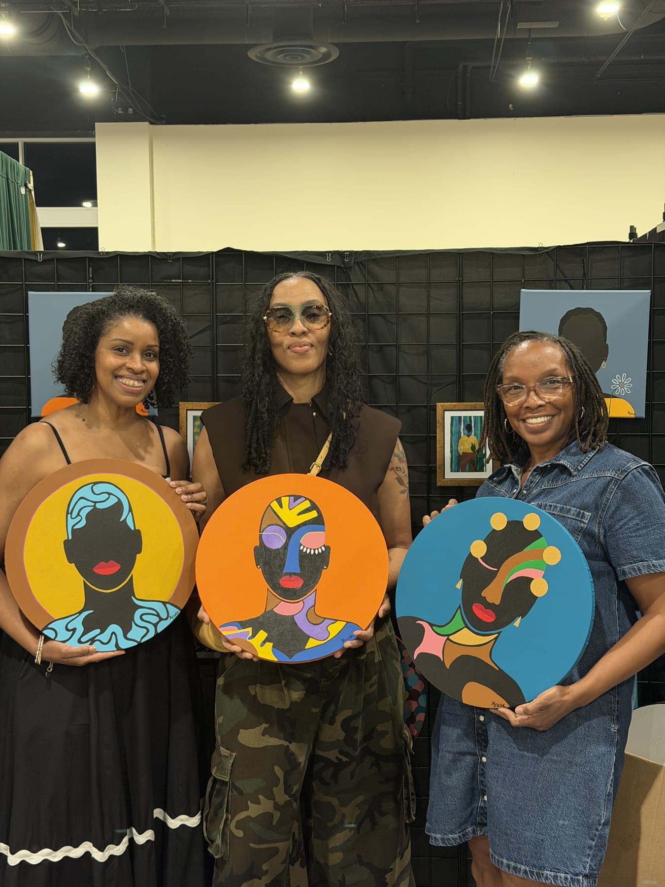 Grace Vieira, right, with two women holding three of her round paintings at an event